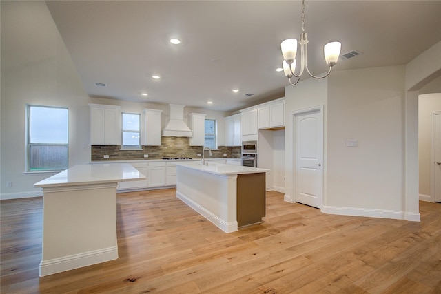 kitchen with premium range hood, a kitchen island with sink, and light countertops