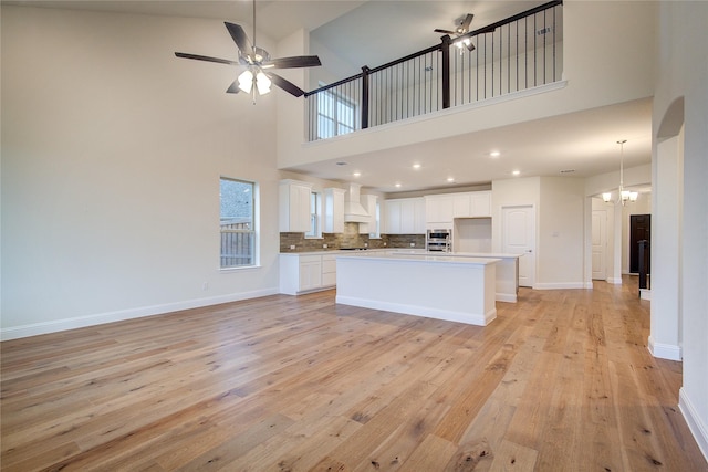 kitchen with ceiling fan with notable chandelier, a kitchen island, white cabinetry, and custom range hood