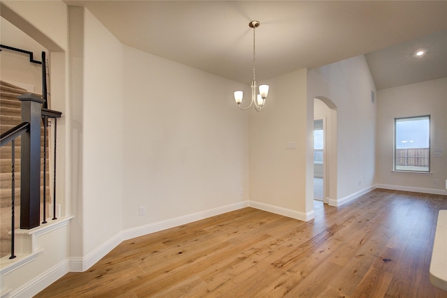 empty room with a chandelier, arched walkways, light wood-style flooring, baseboards, and stairway