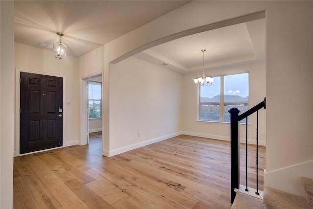 foyer entrance featuring arched walkways, a raised ceiling, light wood-style flooring, stairway, and a mountain view