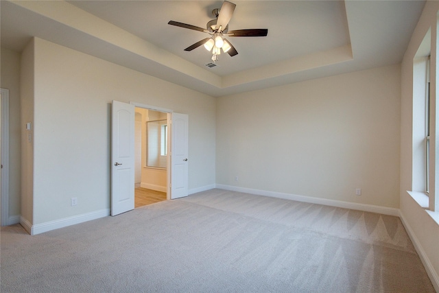 unfurnished room featuring light carpet, baseboards, visible vents, a raised ceiling, and ceiling fan