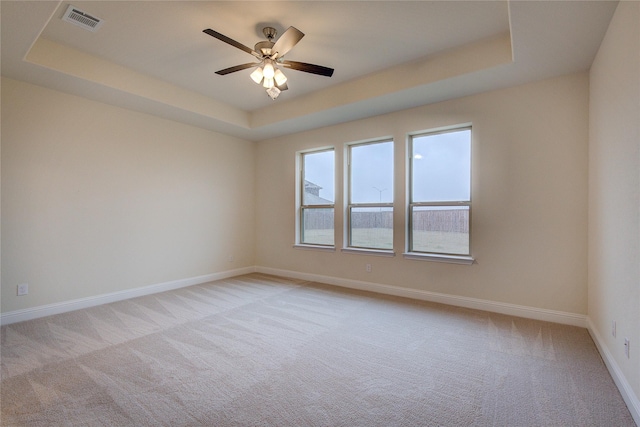 unfurnished room featuring light carpet, visible vents, a tray ceiling, and baseboards