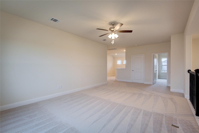 empty room featuring a ceiling fan, light colored carpet, visible vents, and baseboards