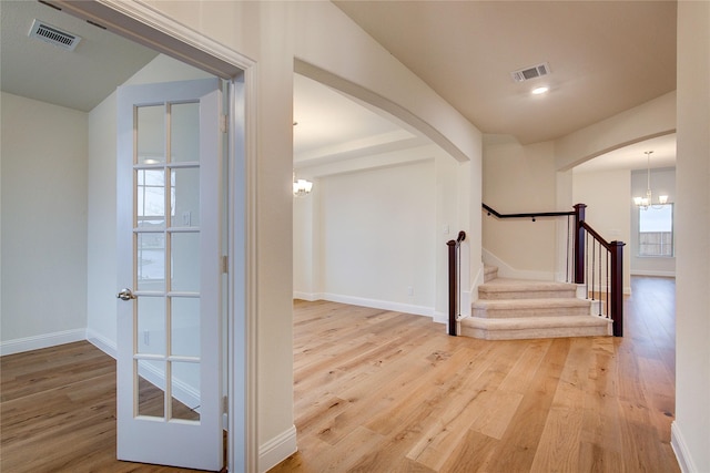 hall featuring light wood finished floors, visible vents, arched walkways, stairs, and a chandelier