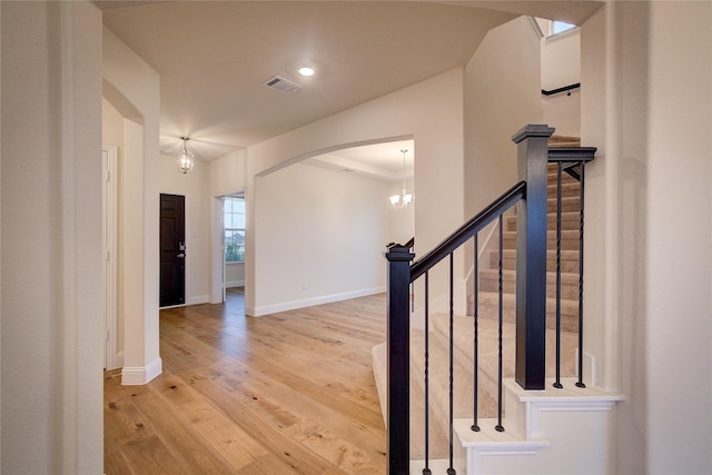 hallway with visible vents, arched walkways, baseboards, light wood-style flooring, and stairs