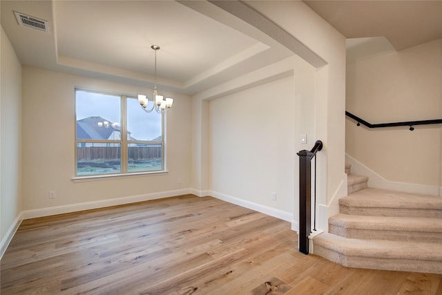 unfurnished dining area featuring a tray ceiling, a notable chandelier, visible vents, stairway, and light wood-style floors