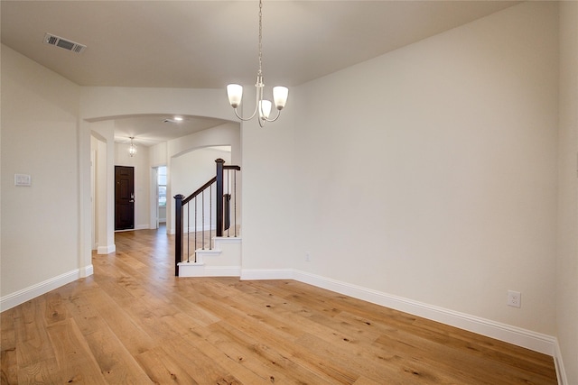 spare room featuring arched walkways, a notable chandelier, light wood finished floors, visible vents, and stairway