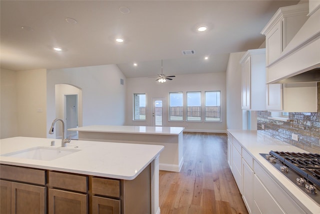 kitchen featuring a kitchen island with sink, light countertops, a sink, and white cabinetry