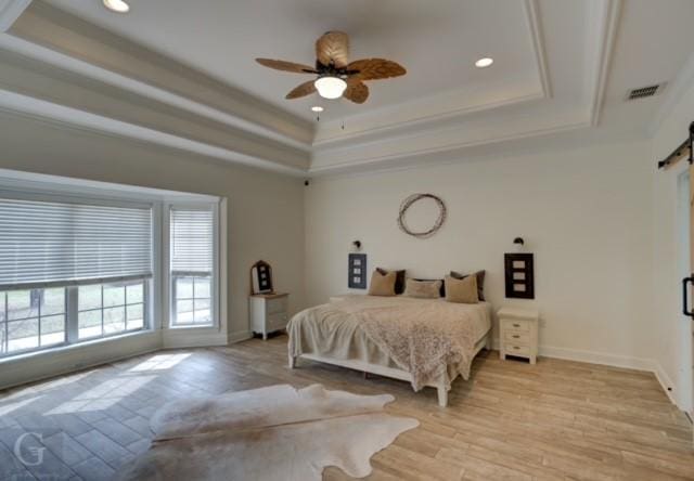 bedroom with a barn door, visible vents, baseboards, light wood-style floors, and a raised ceiling