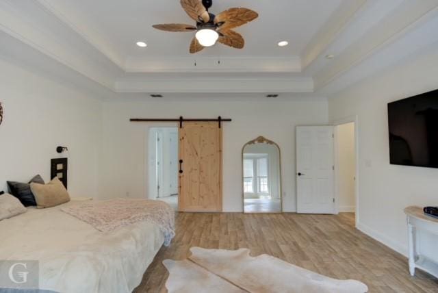 bedroom featuring a tray ceiling, crown molding, recessed lighting, a barn door, and wood finished floors