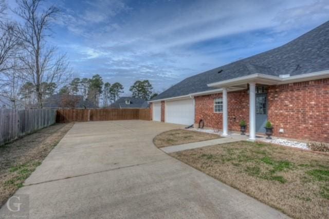 view of side of home with a garage, fence, concrete driveway, and brick siding