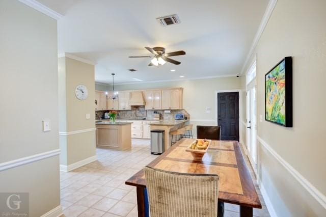 dining space with light tile patterned floors, baseboards, visible vents, a ceiling fan, and crown molding