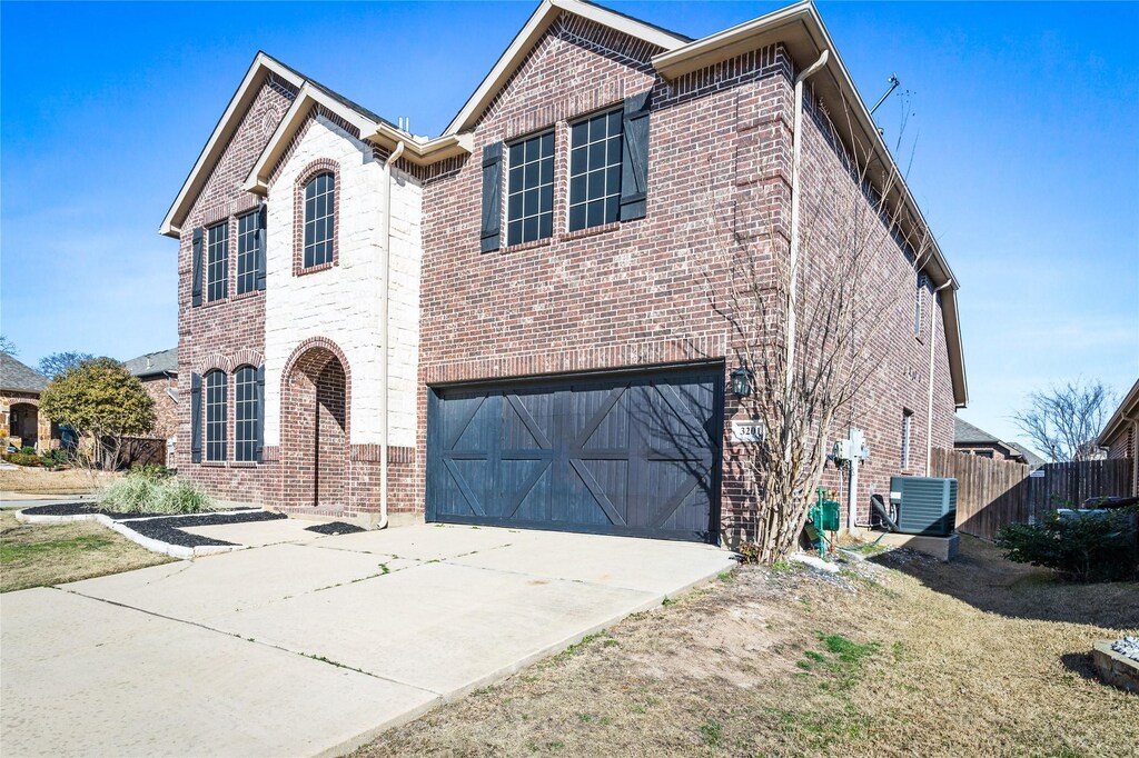 traditional home featuring driveway, brick siding, an attached garage, and fence
