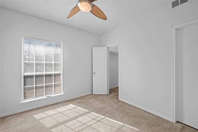 unfurnished bedroom featuring light colored carpet, visible vents, a spacious closet, a textured ceiling, and baseboards