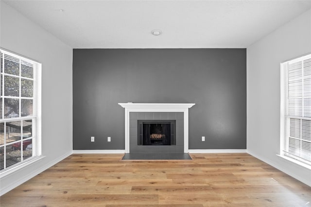 unfurnished living room featuring a wealth of natural light, light wood-style flooring, and a tiled fireplace