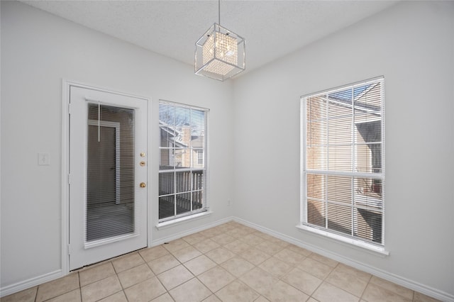 unfurnished dining area featuring a textured ceiling, light tile patterned floors, and baseboards