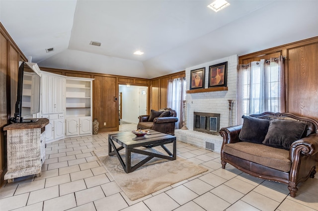 living room with light tile patterned floors, wooden walls, visible vents, vaulted ceiling, and a fireplace