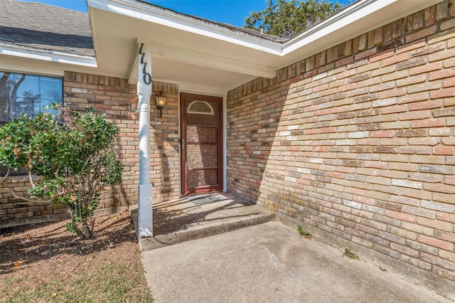 entrance to property with brick siding and a shingled roof