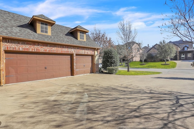 view of side of home featuring a garage, a shingled roof, concrete driveway, and brick siding