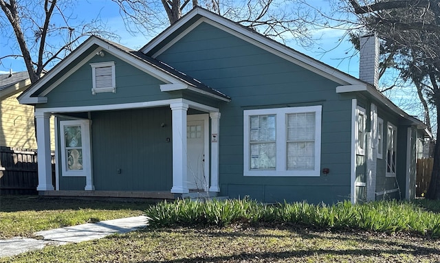 view of front of home with covered porch, fence, and a chimney