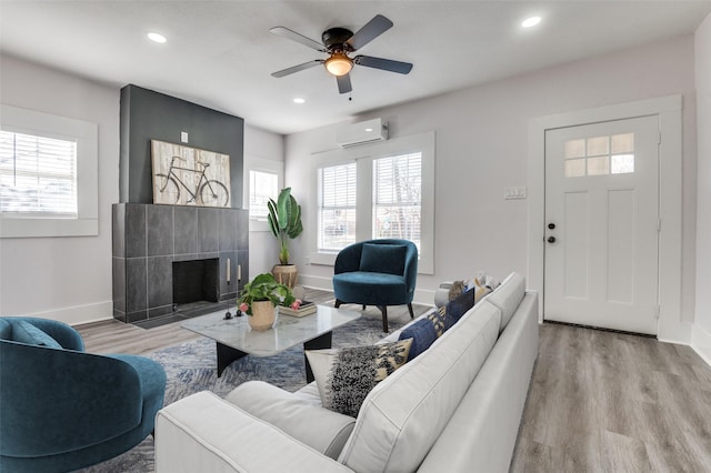 living room featuring a wealth of natural light, a tile fireplace, a wall mounted AC, and wood finished floors