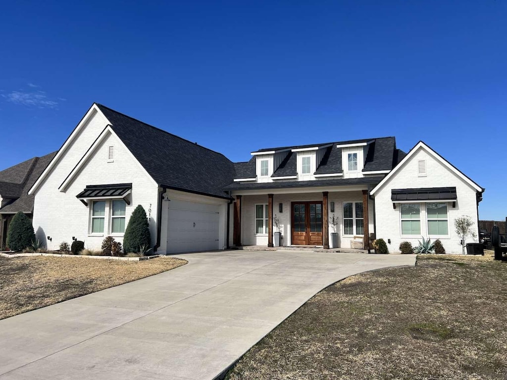 view of front facade featuring a garage, concrete driveway, roof with shingles, french doors, and brick siding