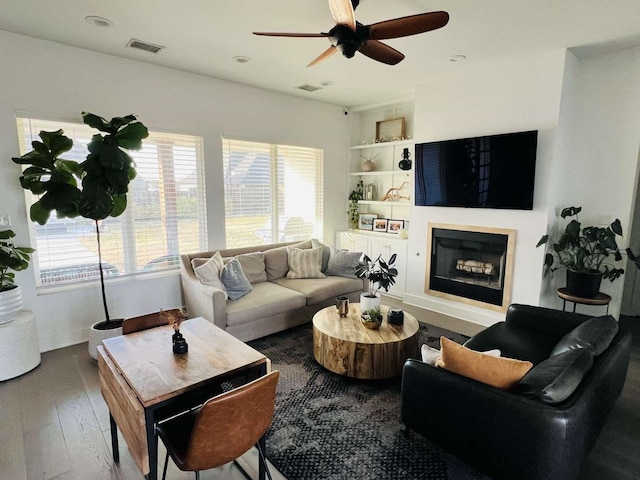 living area with visible vents, built in features, ceiling fan, hardwood / wood-style floors, and a fireplace