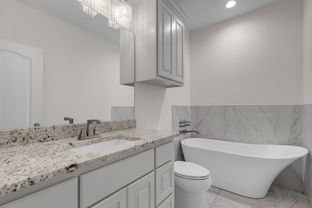 bathroom featuring marble finish floor, recessed lighting, toilet, vanity, and a freestanding tub