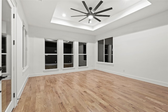 empty room featuring baseboards, a ceiling fan, a tray ceiling, light wood-style floors, and recessed lighting