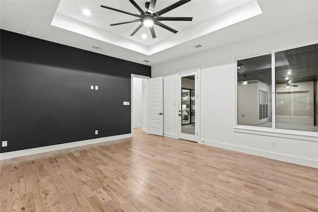 unfurnished room with visible vents, baseboards, ceiling fan, a tray ceiling, and light wood-style floors