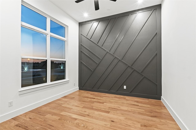 empty room with light wood-style flooring, baseboards, a decorative wall, and a ceiling fan