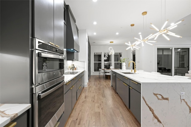 kitchen with a large island, hanging light fixtures, appliances with stainless steel finishes, a sink, and wall chimney exhaust hood