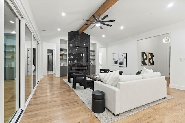 living room featuring a fireplace, light wood-style floors, ceiling fan, beamed ceiling, and baseboards