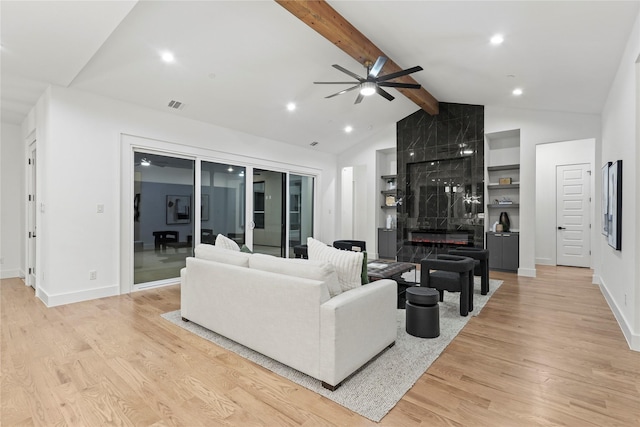 living area featuring vaulted ceiling with beams, light wood-style flooring, a high end fireplace, visible vents, and baseboards