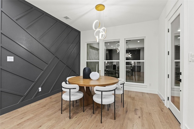 dining room with light wood-style floors, visible vents, a decorative wall, and an inviting chandelier