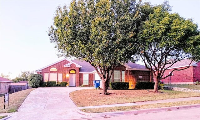 view of front of property featuring brick siding, driveway, and fence