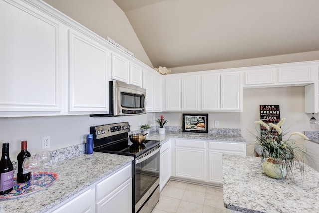 kitchen with light tile patterned floors, light stone counters, white cabinetry, vaulted ceiling, and appliances with stainless steel finishes