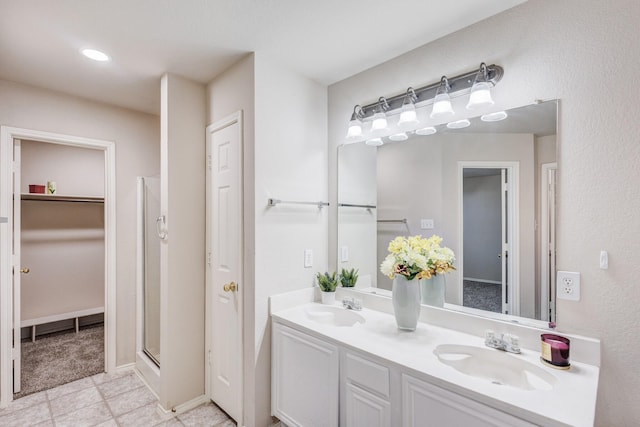 full bathroom featuring double vanity, a shower stall, a walk in closet, and a sink