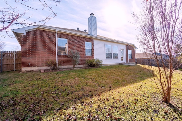 rear view of house with a yard, a chimney, fence, and brick siding