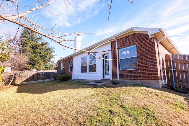 rear view of property with entry steps, brick siding, fence, a yard, and a chimney