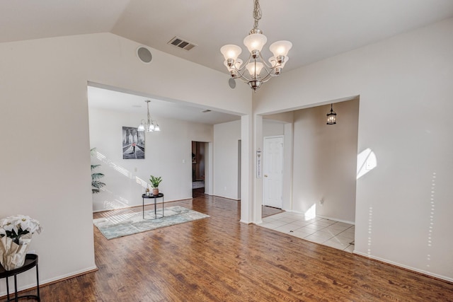 interior space with a chandelier, vaulted ceiling, wood finished floors, and visible vents