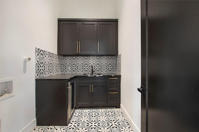 bar featuring light tile patterned floors, decorative backsplash, a sink, a bar, and baseboards