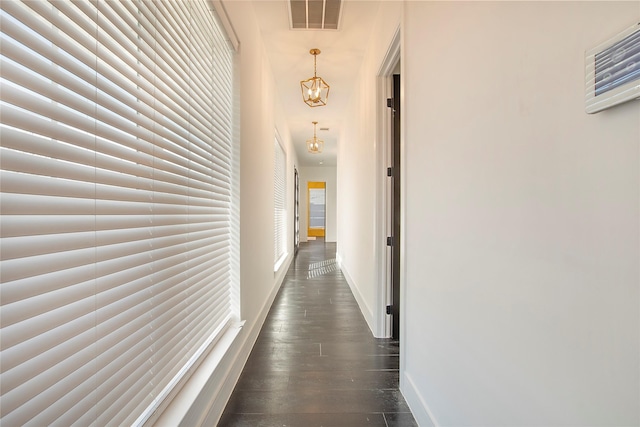 corridor featuring dark wood-style floors, an inviting chandelier, visible vents, and baseboards