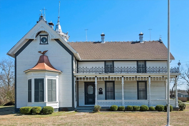 victorian house with covered porch, a shingled roof, a front yard, and a balcony