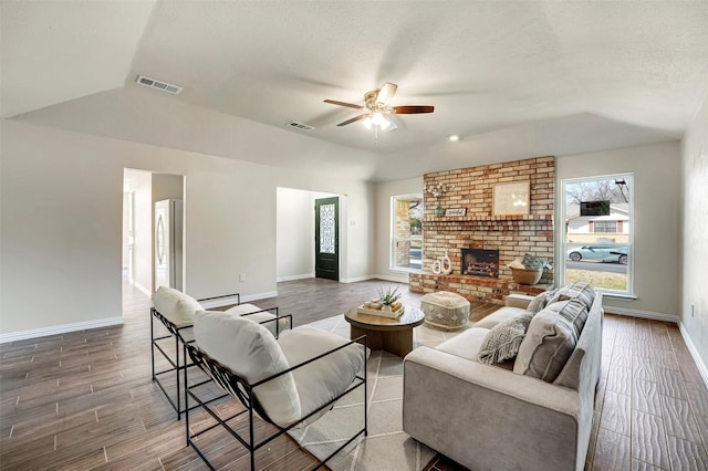 living area with a textured ceiling, a brick fireplace, wood finished floors, and visible vents