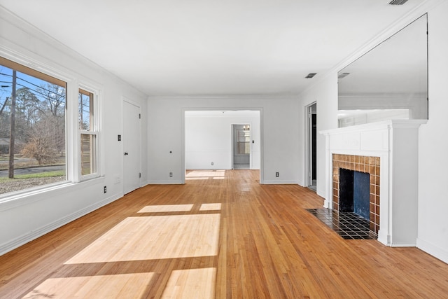 unfurnished living room with light wood finished floors, a tiled fireplace, visible vents, and baseboards