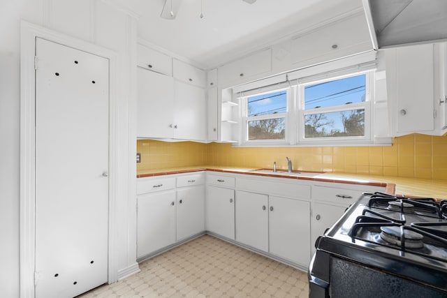 kitchen featuring light floors, light countertops, gas stove, white cabinets, and a sink