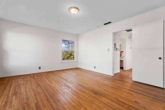 spare room featuring light wood-type flooring, visible vents, and baseboards