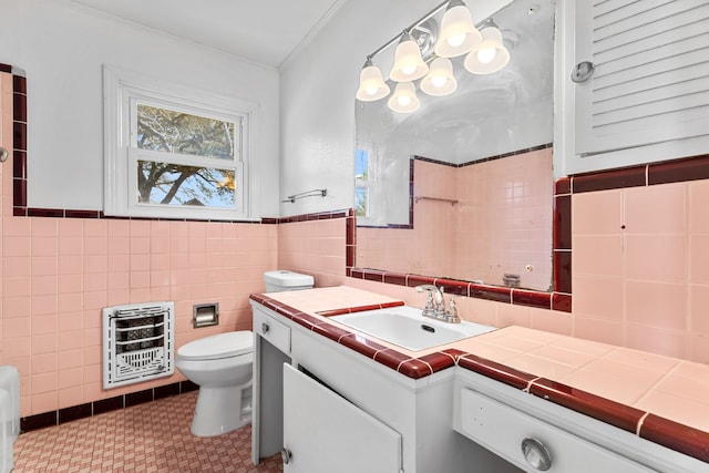 bathroom featuring toilet, tile walls, vanity, heating unit, and crown molding