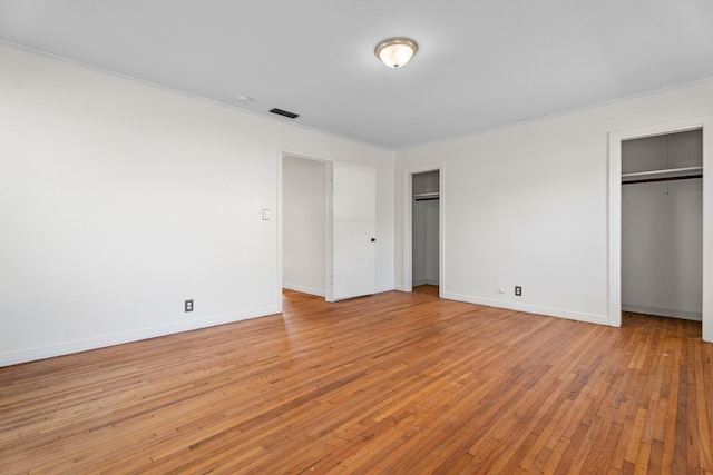 unfurnished bedroom featuring baseboards, light wood finished floors, visible vents, and multiple closets